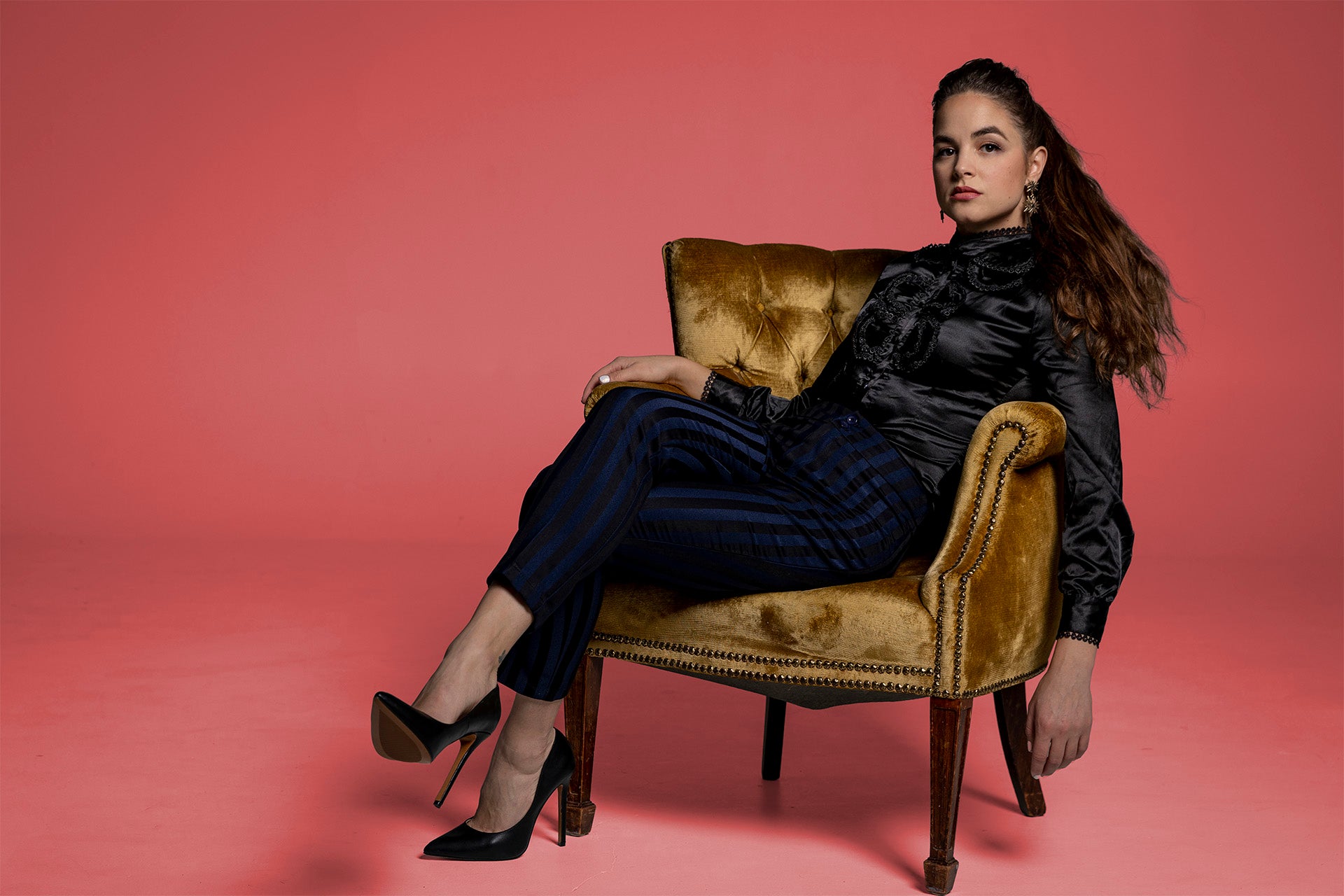 Calysta sitting on a vintage chair against a pink background